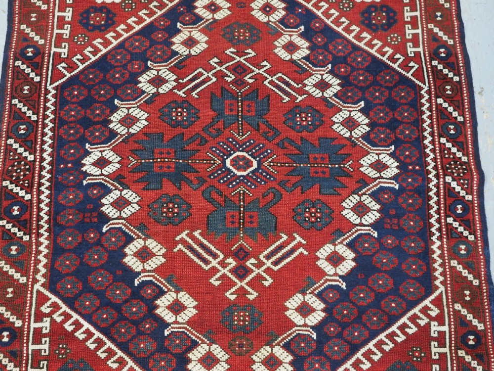 An antique hand-knotted Turkish Kiz Bergama wool rug featuring a red field, central diamond medallion, navy blue accents, and geometric borders. View IV