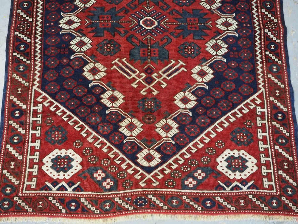 An antique hand-knotted Turkish Kiz Bergama wool rug featuring a red field, central diamond medallion, navy blue accents, and geometric borders. View V