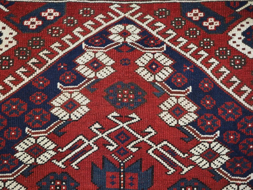 An antique hand-knotted Turkish Kiz Bergama wool rug featuring a red field, central diamond medallion, navy blue accents, and geometric borders. View VI
