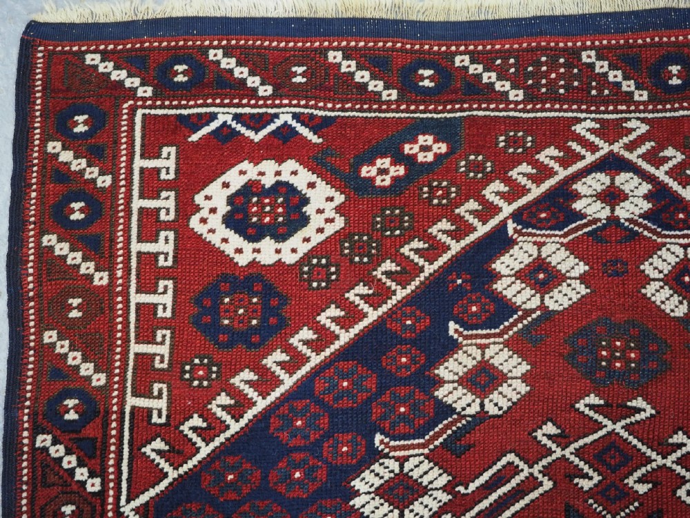 An antique hand-knotted Turkish Kiz Bergama wool rug featuring a red field, central diamond medallion, navy blue accents, and geometric borders. View IX