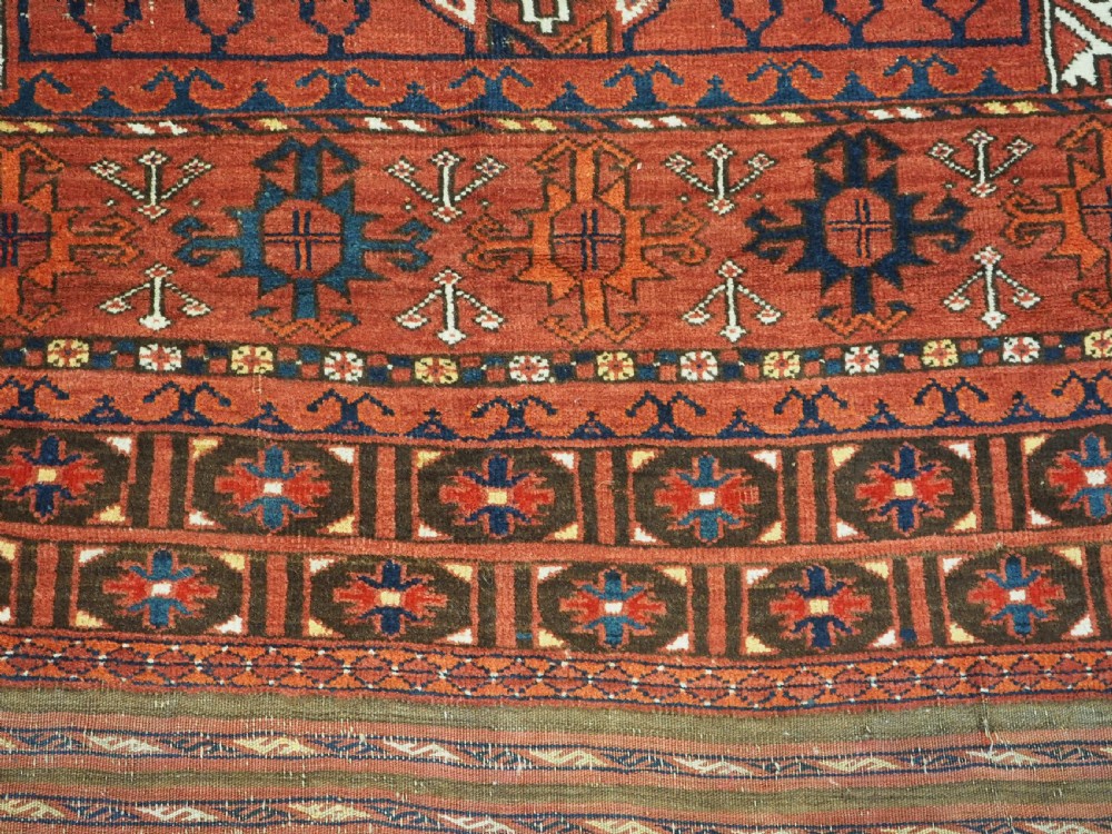 An antique hand-knotted Ersari Turkmen Ensi wool rug featuring deep red tones, a central cruciform design, geometric borders, and a woven fringe. View X