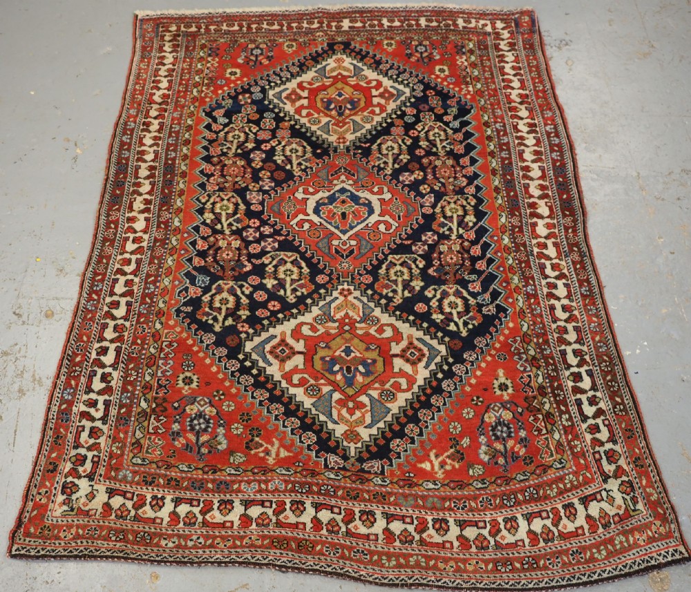 An antique hand-knotted Qashqai wool rug featuring a navy blue field with stacked diamond medallions surrounded by terracotta red borders and tribal geometric motifs.