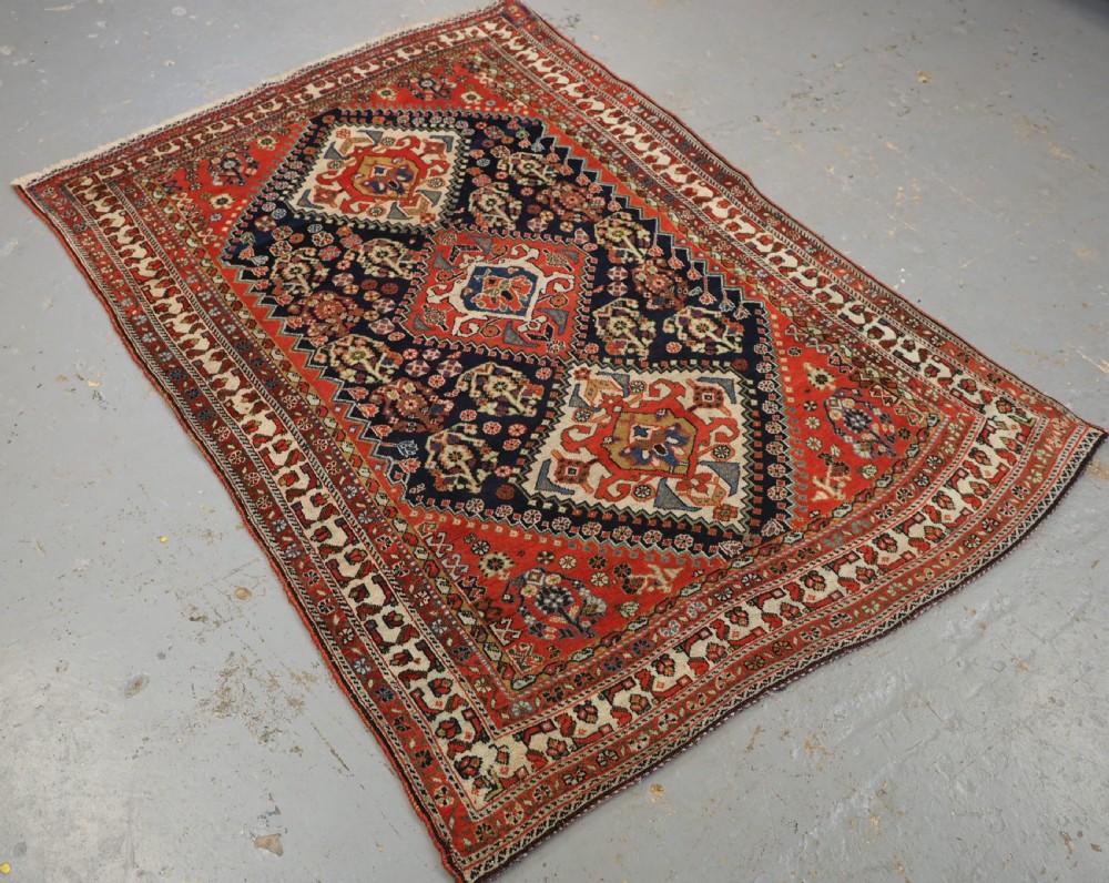 An antique hand-knotted Qashqai wool rug featuring a navy blue field with stacked diamond medallions surrounded by terracotta red borders and tribal geometric motifs. View II