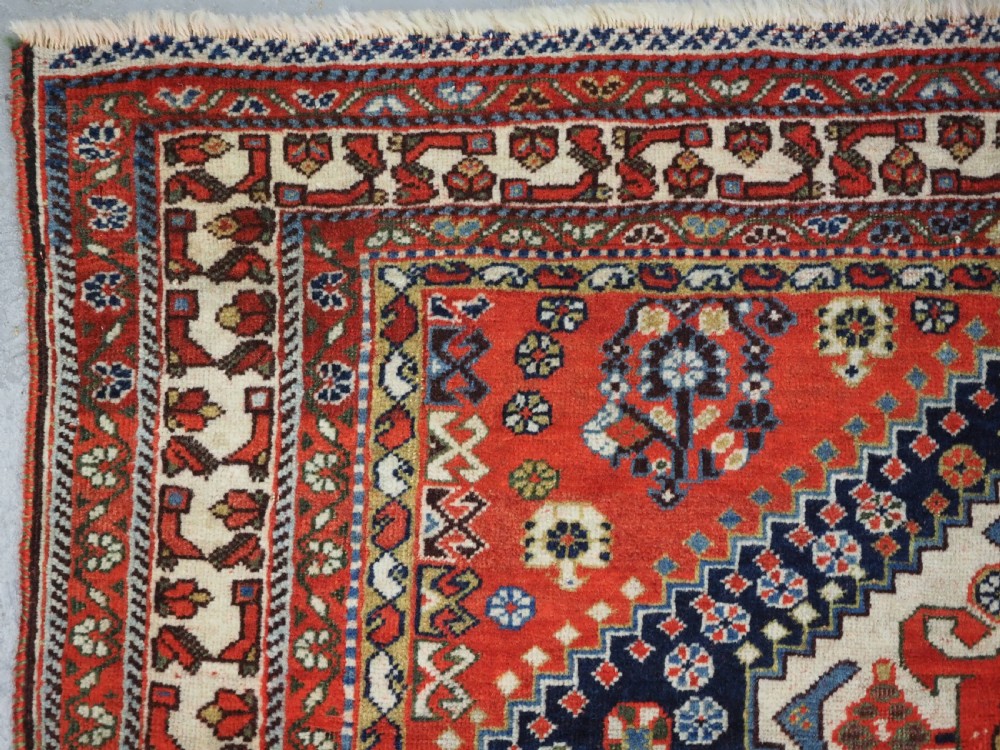 An antique hand-knotted Qashqai wool rug featuring a navy blue field with stacked diamond medallions surrounded by terracotta red borders and tribal geometric motifs. View VI