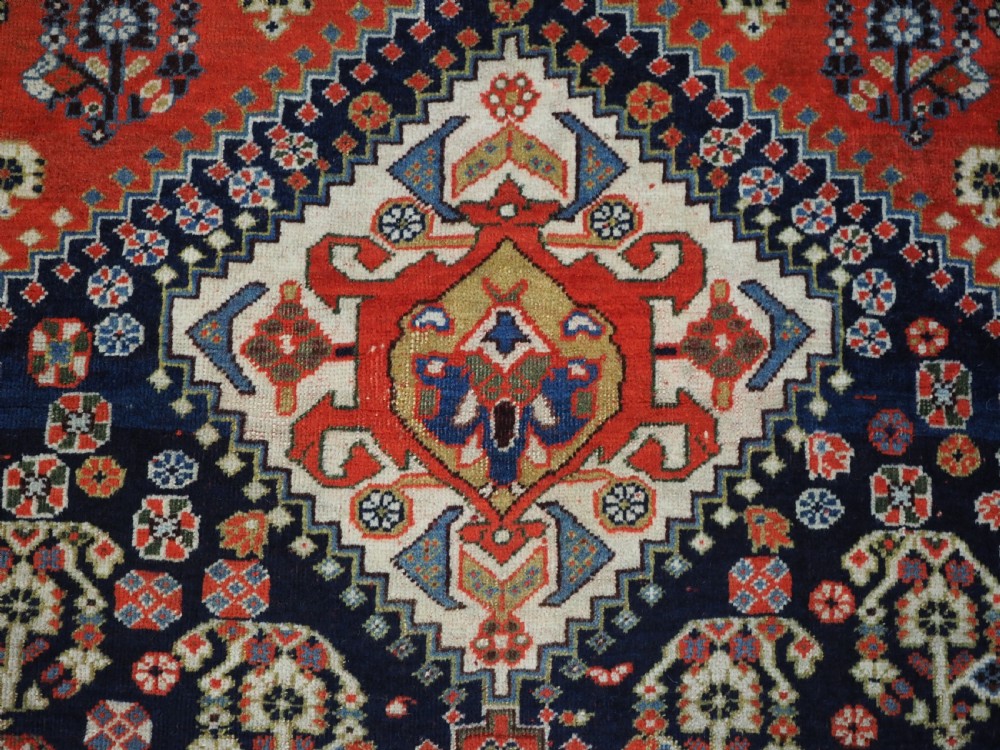 An antique hand-knotted Qashqai wool rug featuring a navy blue field with stacked diamond medallions surrounded by terracotta red borders and tribal geometric motifs. View VII