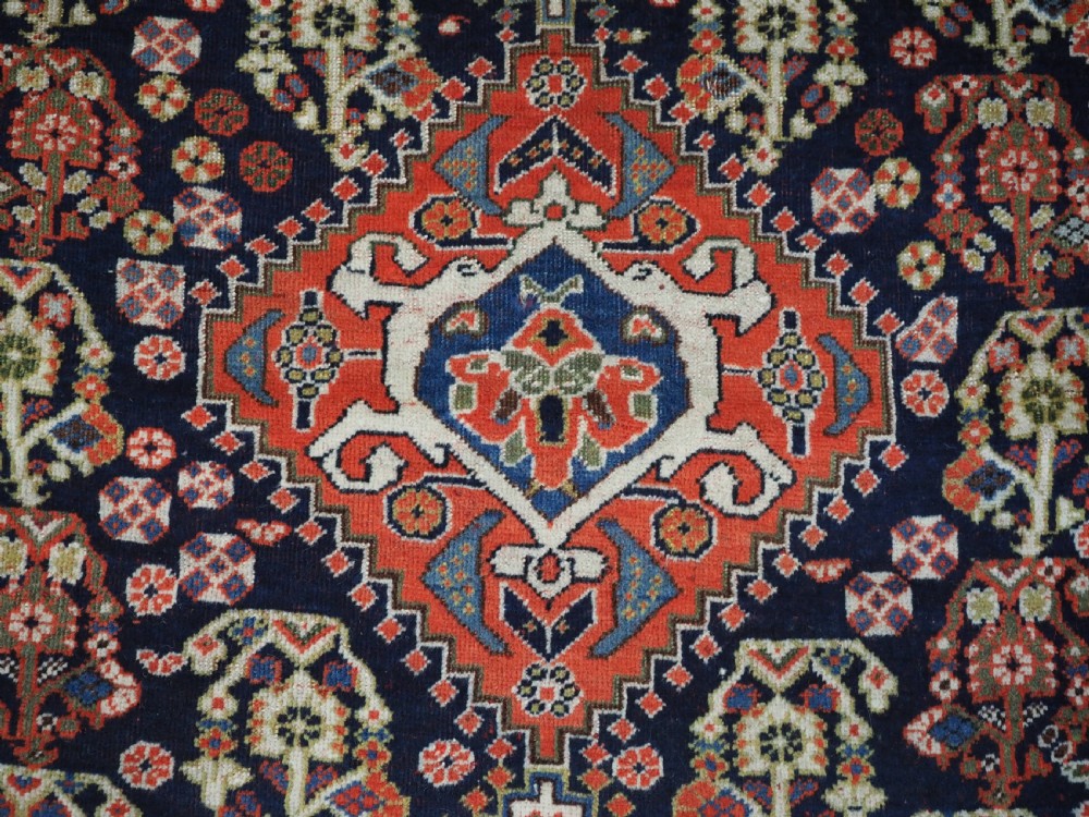 An antique hand-knotted Qashqai wool rug featuring a navy blue field with stacked diamond medallions surrounded by terracotta red borders and tribal geometric motifs. View VIII
