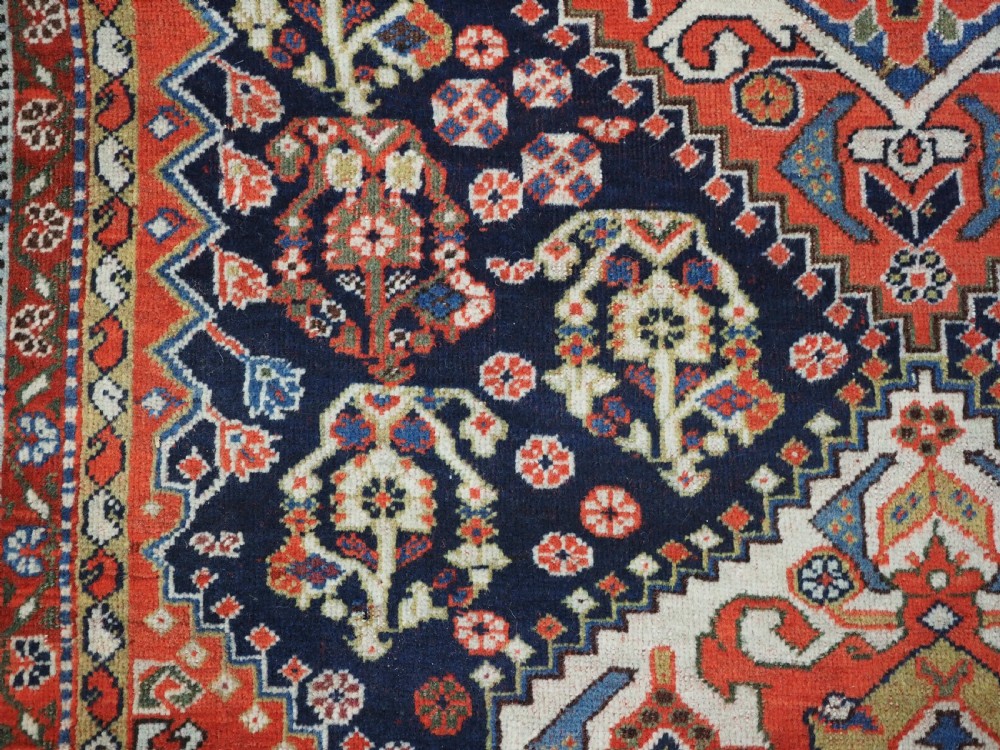 An antique hand-knotted Qashqai wool rug featuring a navy blue field with stacked diamond medallions surrounded by terracotta red borders and tribal geometric motifs. View XI