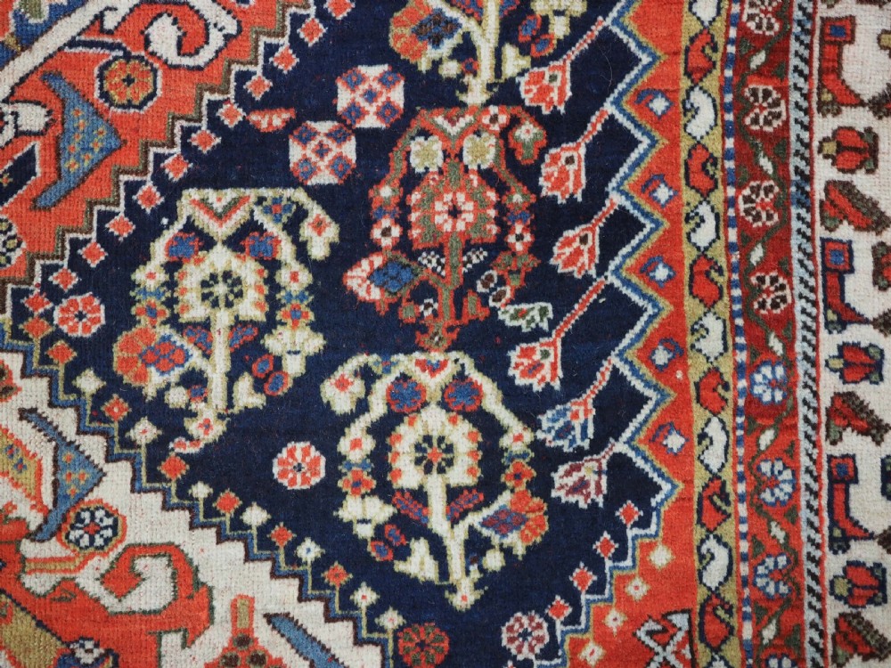 An antique hand-knotted Qashqai wool rug featuring a navy blue field with stacked diamond medallions surrounded by terracotta red borders and tribal geometric motifs. View XII