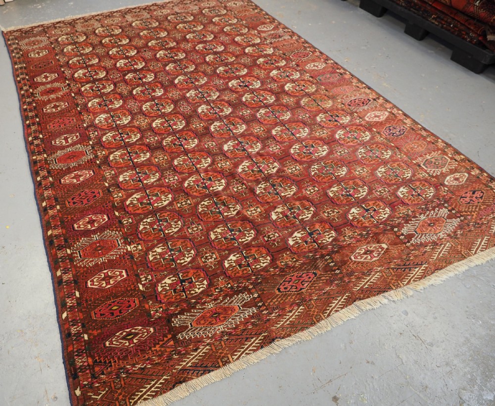 An antique Tekke Turkmen wool area rug featuring a repeating grid of octagonal gol motifs on a deep rust-red field with decorative geometric borders. View II