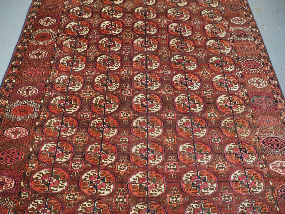 An antique Tekke Turkmen wool area rug featuring a repeating grid of octagonal gol motifs on a deep rust-red field with decorative geometric borders. View III