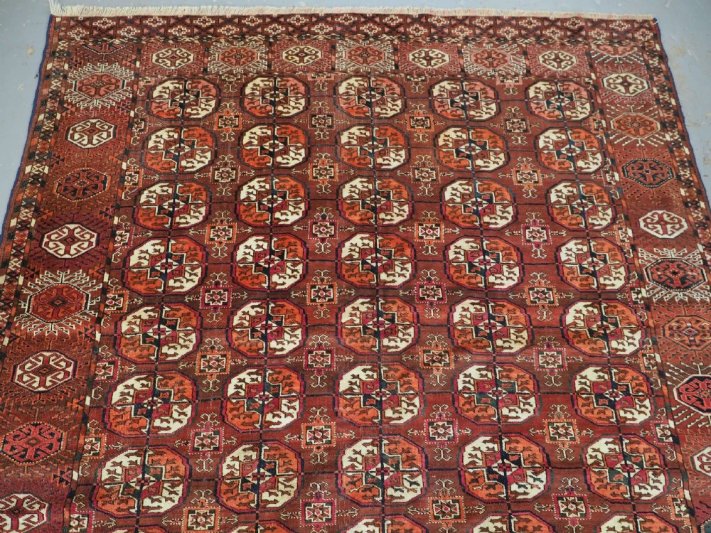 An antique Tekke Turkmen wool area rug featuring a repeating grid of octagonal gol motifs on a deep rust-red field with decorative geometric borders. View IV