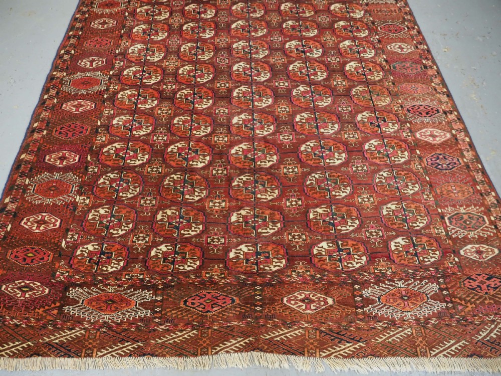 An antique Tekke Turkmen wool area rug featuring a repeating grid of octagonal gol motifs on a deep rust-red field with decorative geometric borders. View V