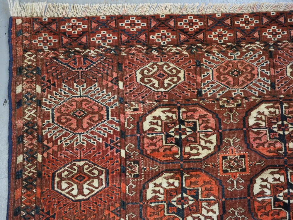 An antique Tekke Turkmen wool area rug featuring a repeating grid of octagonal gol motifs on a deep rust-red field with decorative geometric borders. View VI