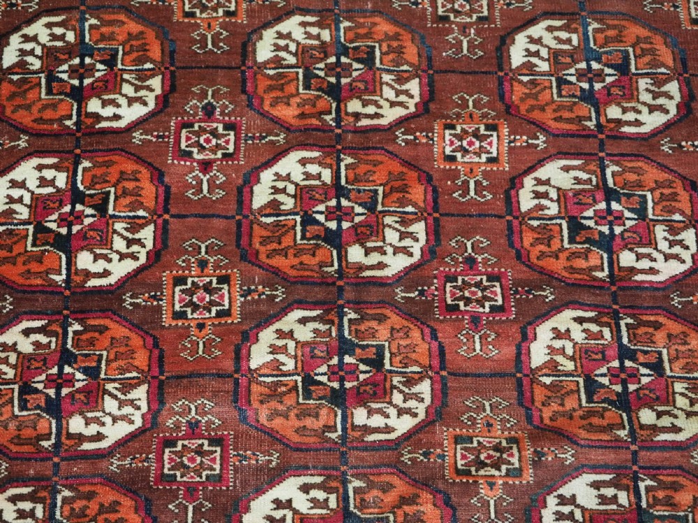 An antique Tekke Turkmen wool area rug featuring a repeating grid of octagonal gol motifs on a deep rust-red field with decorative geometric borders. View VIII