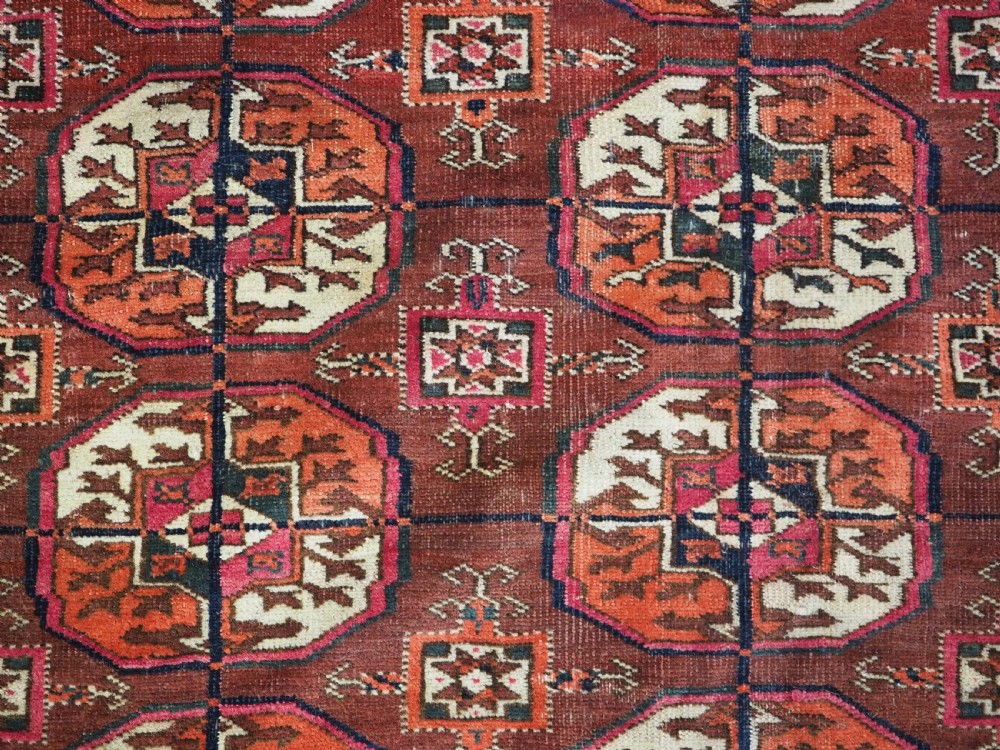 An antique Tekke Turkmen wool area rug featuring a repeating grid of octagonal gol motifs on a deep rust-red field with decorative geometric borders. View IX