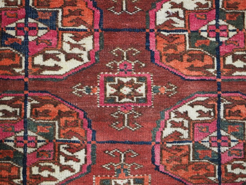 An antique Tekke Turkmen wool area rug featuring a repeating grid of octagonal gol motifs on a deep rust-red field with decorative geometric borders. View X