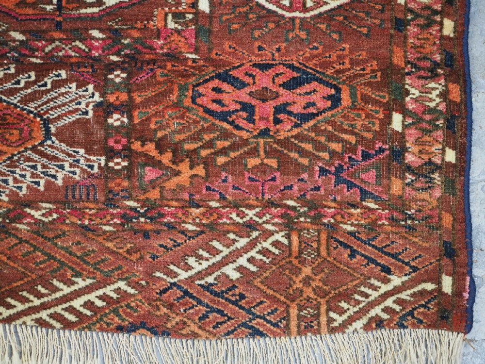 An antique Tekke Turkmen wool area rug featuring a repeating grid of octagonal gol motifs on a deep rust-red field with decorative geometric borders. View XI