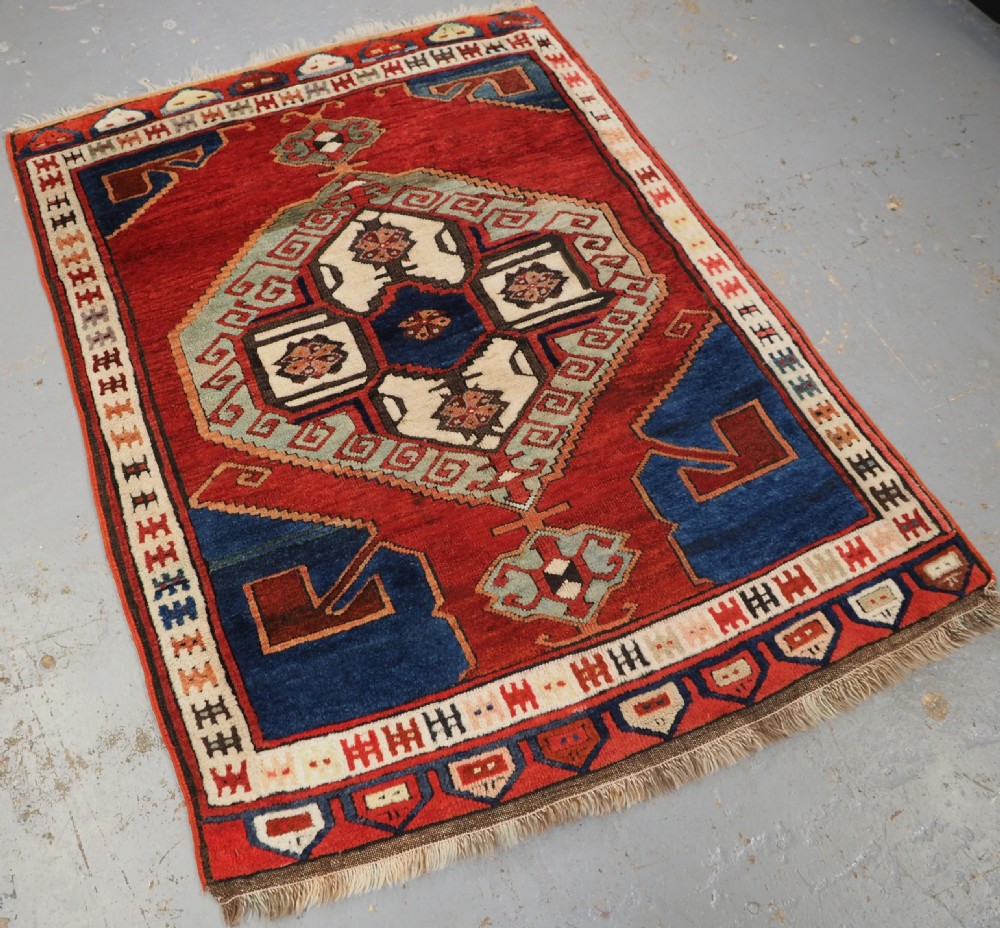 An antique 19th-century Turkish Karapinar wool rug featuring a central geometric medallion in blue, green, and cream set against a deep red ground field with multi-coloured geometric borders. View II