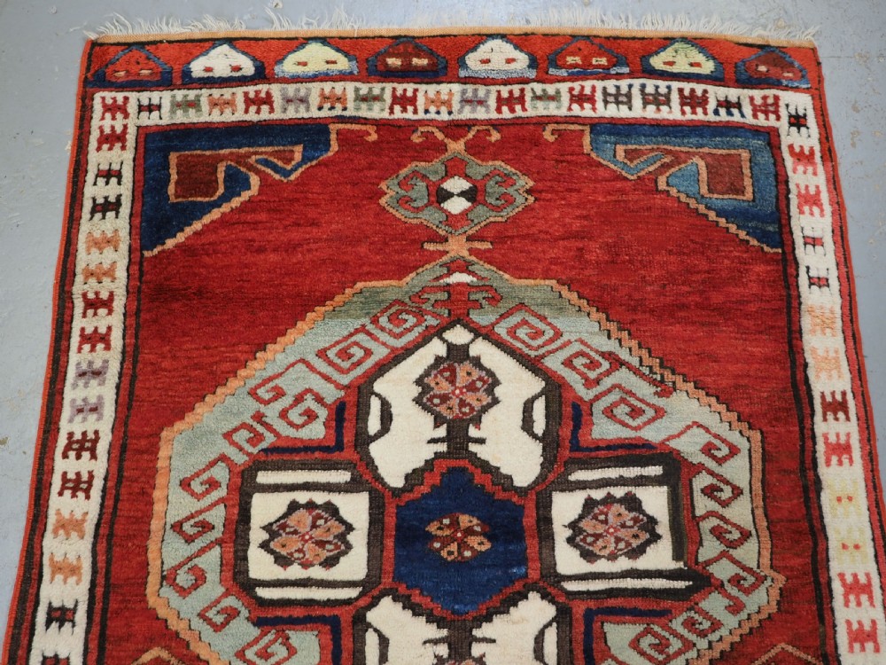 An antique 19th-century Turkish Karapinar wool rug featuring a central geometric medallion in blue, green, and cream set against a deep red ground field with multi-coloured geometric borders. View III