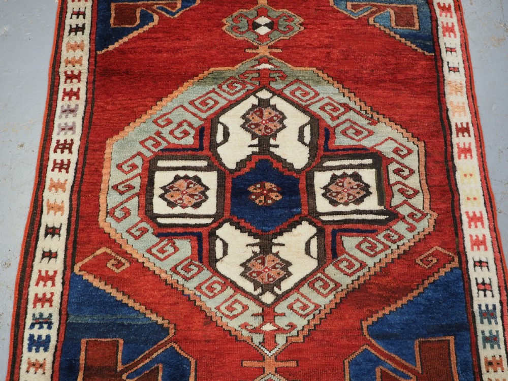 An antique 19th-century Turkish Karapinar wool rug featuring a central geometric medallion in blue, green, and cream set against a deep red ground field with multi-coloured geometric borders. View IV