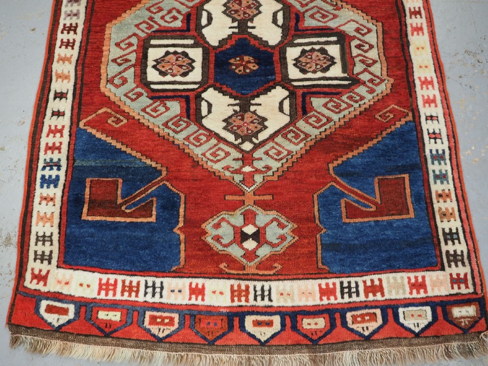 An antique 19th-century Turkish Karapinar wool rug featuring a central geometric medallion in blue, green, and cream set against a deep red ground field with multi-coloured geometric borders. View V