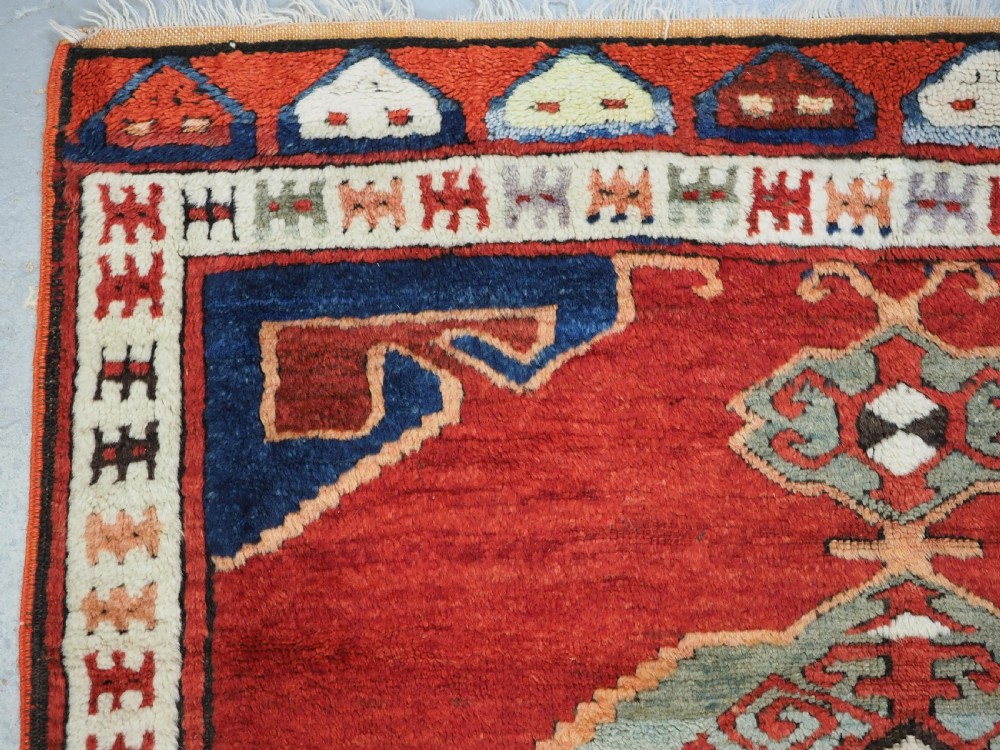 An antique 19th-century Turkish Karapinar wool rug featuring a central geometric medallion in blue, green, and cream set against a deep red ground field with multi-coloured geometric borders. View VI