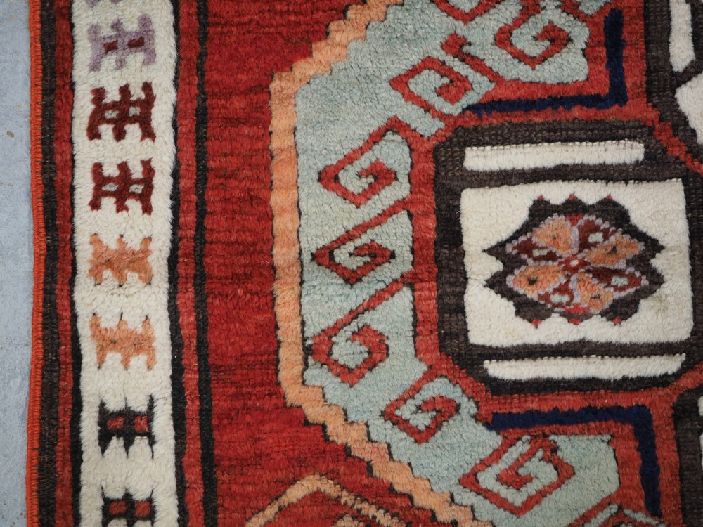 An antique 19th-century Turkish Karapinar wool rug featuring a central geometric medallion in blue, green, and cream set against a deep red ground field with multi-coloured geometric borders. View VII
