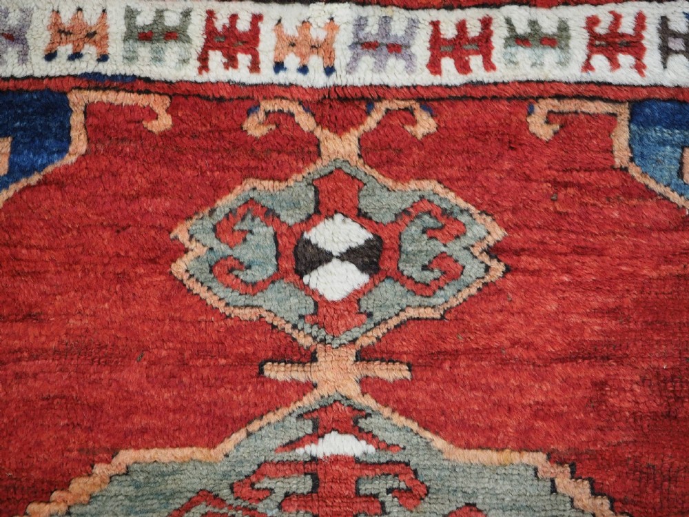 An antique 19th-century Turkish Karapinar wool rug featuring a central geometric medallion in blue, green, and cream set against a deep red ground field with multi-coloured geometric borders. View VIII