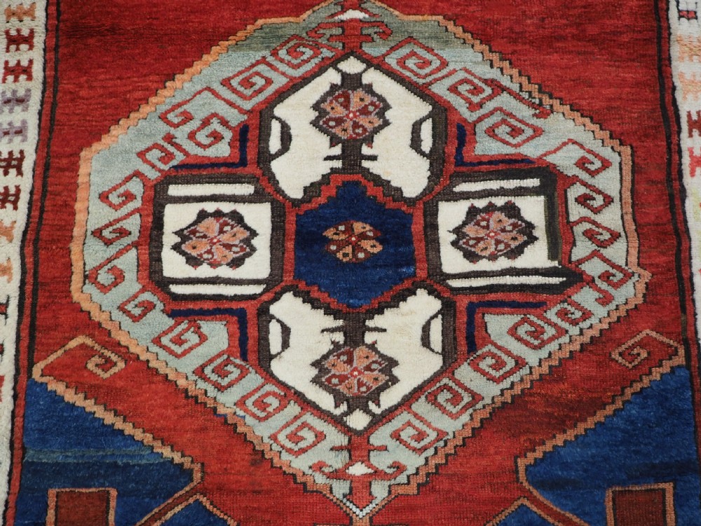 An antique 19th-century Turkish Karapinar wool rug featuring a central geometric medallion in blue, green, and cream set against a deep red ground field with multi-coloured geometric borders. View IX