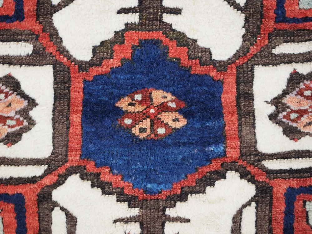 An antique 19th-century Turkish Karapinar wool rug featuring a central geometric medallion in blue, green, and cream set against a deep red ground field with multi-coloured geometric borders. View X