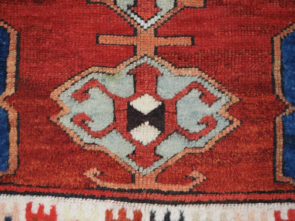 An antique 19th-century Turkish Karapinar wool rug featuring a central geometric medallion in blue, green, and cream set against a deep red ground field with multi-coloured geometric borders. View XI