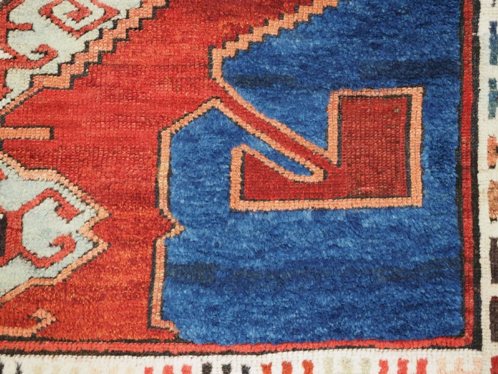An antique 19th-century Turkish Karapinar wool rug featuring a central geometric medallion in blue, green, and cream set against a deep red ground field with multi-coloured geometric borders. View XII