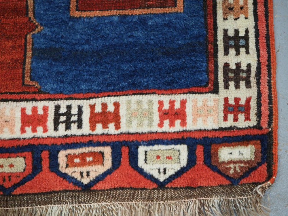 An antique 19th-century Turkish Karapinar wool rug featuring a central geometric medallion in blue, green, and cream set against a deep red ground field with multi-coloured geometric borders. View XIII