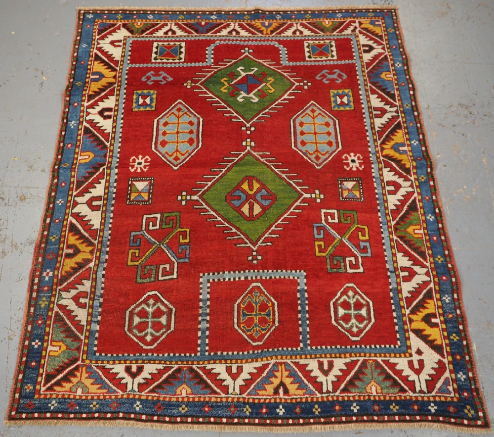 An antique hand-knotted Caucasian Fachralo Kazak prayer rug featuring a red field with green diamond medallions and a geometric border.