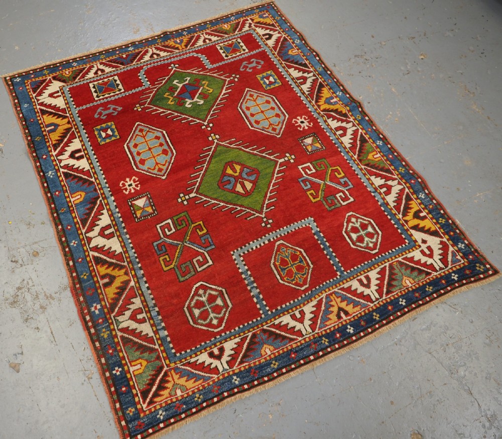 An antique hand-knotted Caucasian Fachralo Kazak prayer rug featuring a red field with green diamond medallions and a geometric border. View II