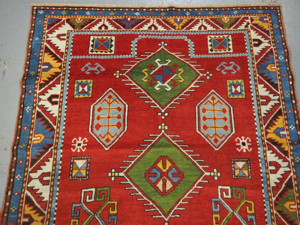 An antique hand-knotted Caucasian Fachralo Kazak prayer rug featuring a red field with green diamond medallions and a geometric border. View III