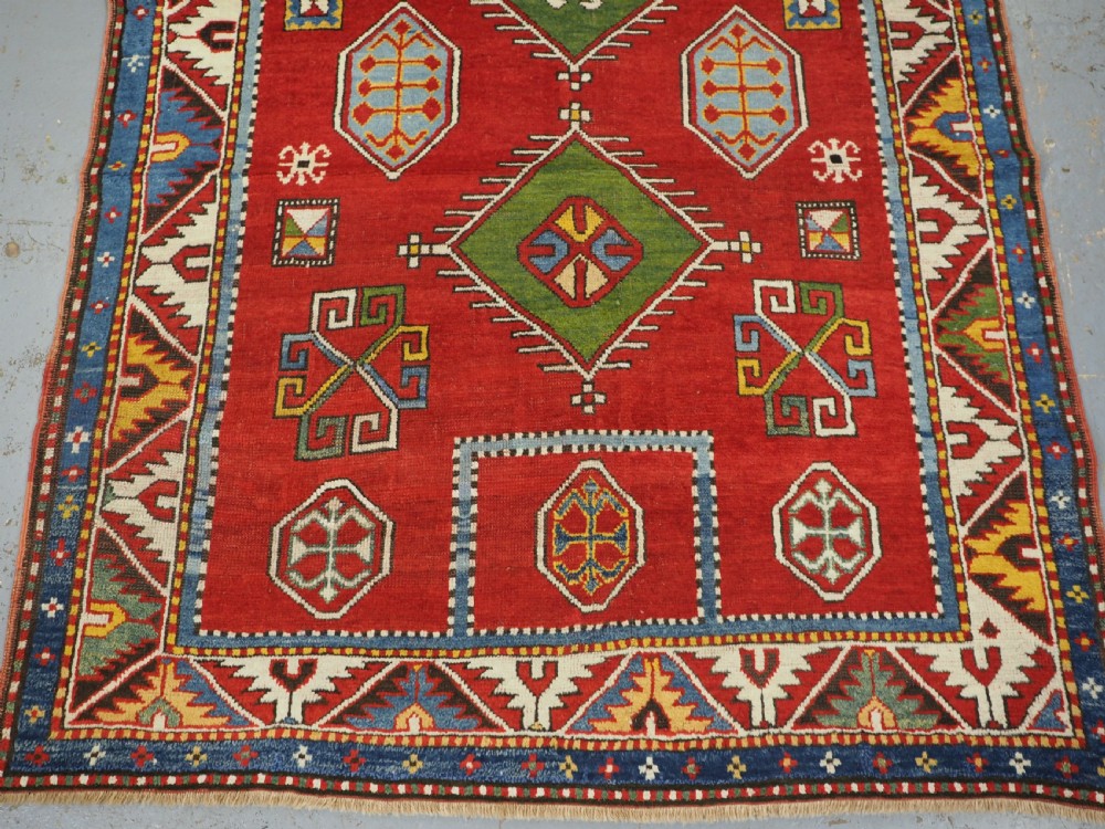 An antique hand-knotted Caucasian Fachralo Kazak prayer rug featuring a red field with green diamond medallions and a geometric border. View IV