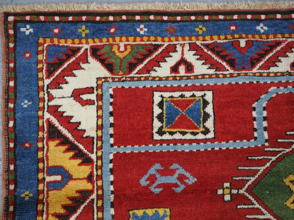 An antique hand-knotted Caucasian Fachralo Kazak prayer rug featuring a red field with green diamond medallions and a geometric border. View V
