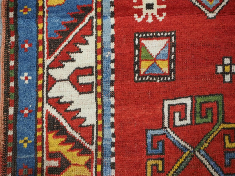 An antique hand-knotted Caucasian Fachralo Kazak prayer rug featuring a red field with green diamond medallions and a geometric border. View VI