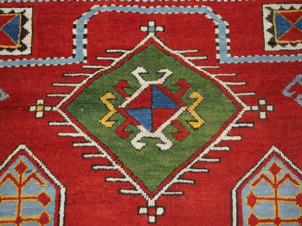 An antique hand-knotted Caucasian Fachralo Kazak prayer rug featuring a red field with green diamond medallions and a geometric border. View VII