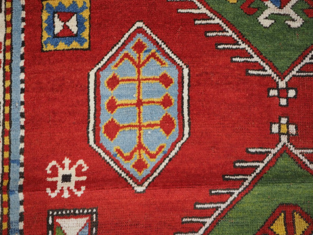 An antique hand-knotted Caucasian Fachralo Kazak prayer rug featuring a red field with green diamond medallions and a geometric border. View VIII