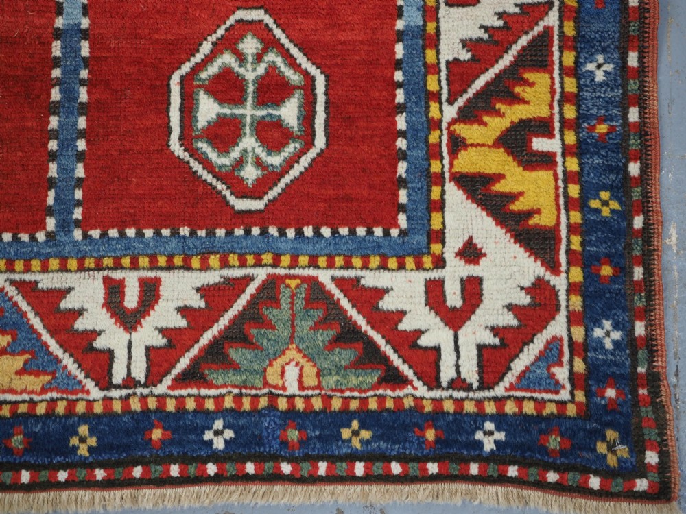 An antique hand-knotted Caucasian Fachralo Kazak prayer rug featuring a red field with green diamond medallions and a geometric border. View X