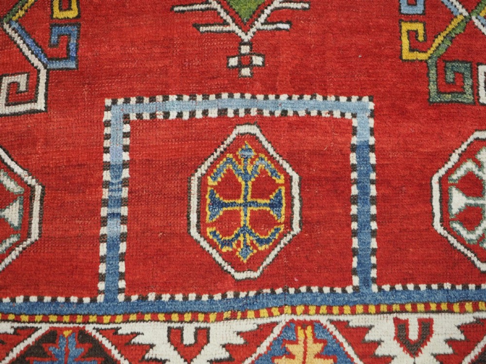 An antique hand-knotted Caucasian Fachralo Kazak prayer rug featuring a red field with green diamond medallions and a geometric border. View XII