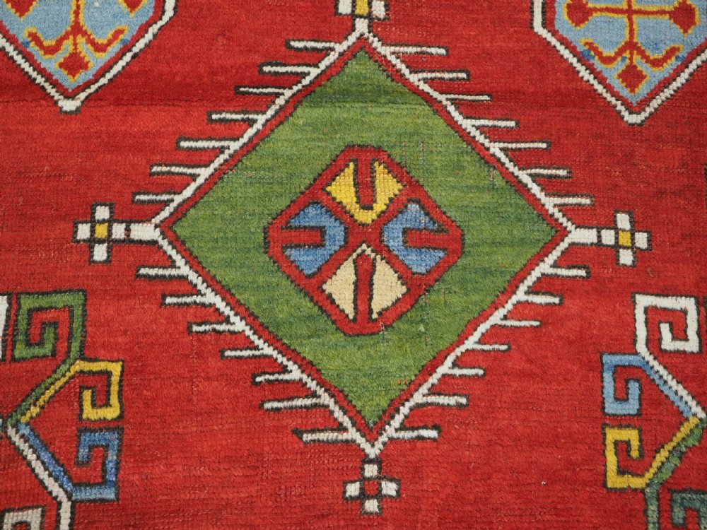 An antique hand-knotted Caucasian Fachralo Kazak prayer rug featuring a red field with green diamond medallions and a geometric border. View XIII