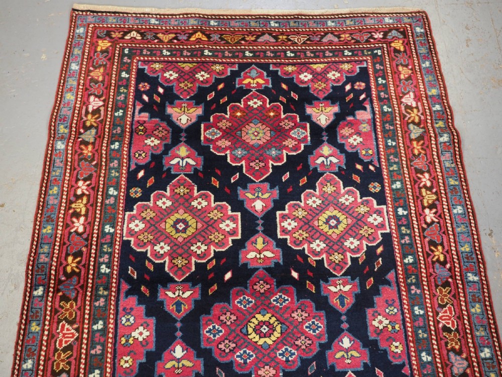An antique long Caucasian runner rug featuring repeating pink and yellow geometric medallions on a dark navy field surrounded by a multi-band decorative border. View III