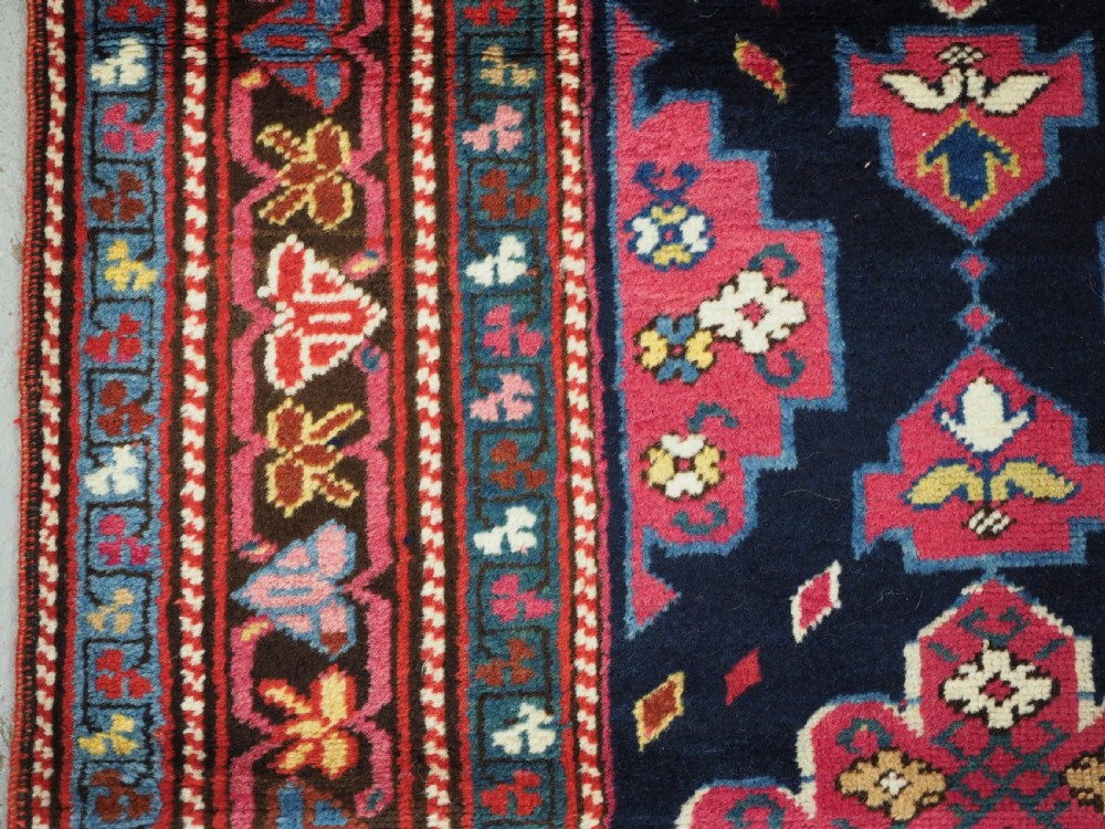 An antique long Caucasian runner rug featuring repeating pink and yellow geometric medallions on a dark navy field surrounded by a multi-band decorative border. View VIII