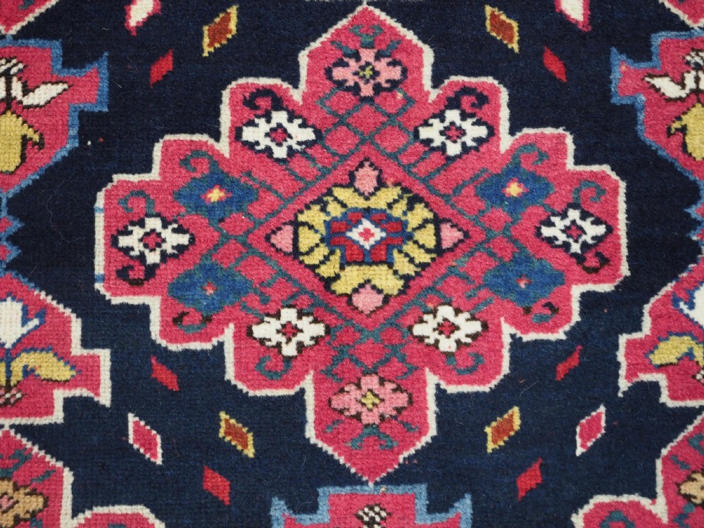 An antique long Caucasian runner rug featuring repeating pink and yellow geometric medallions on a dark navy field surrounded by a multi-band decorative border. View XI