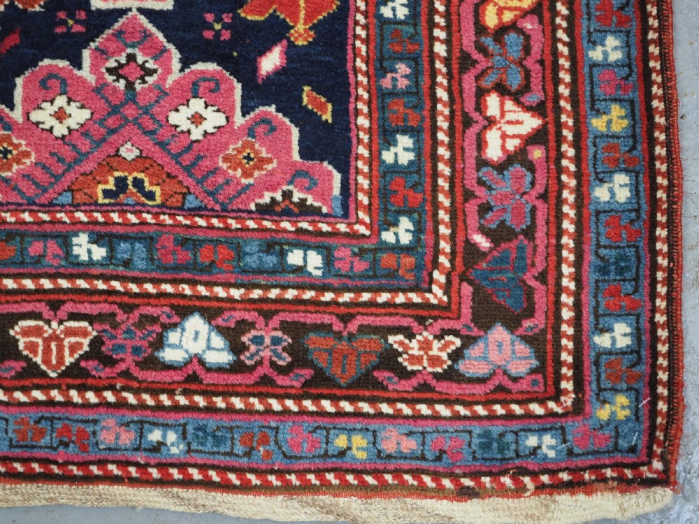 An antique long Caucasian runner rug featuring repeating pink and yellow geometric medallions on a dark navy field surrounded by a multi-band decorative border. View XIII