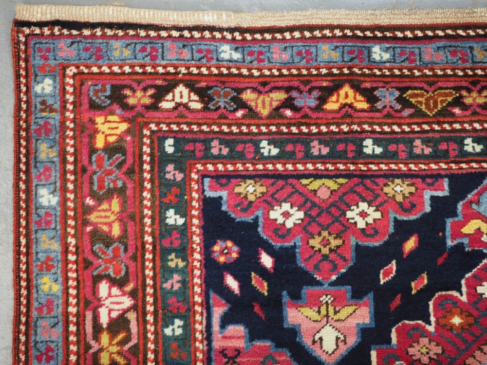 An antique long Caucasian runner rug featuring repeating pink and yellow geometric medallions on a dark navy field surrounded by a multi-band decorative border. View XX