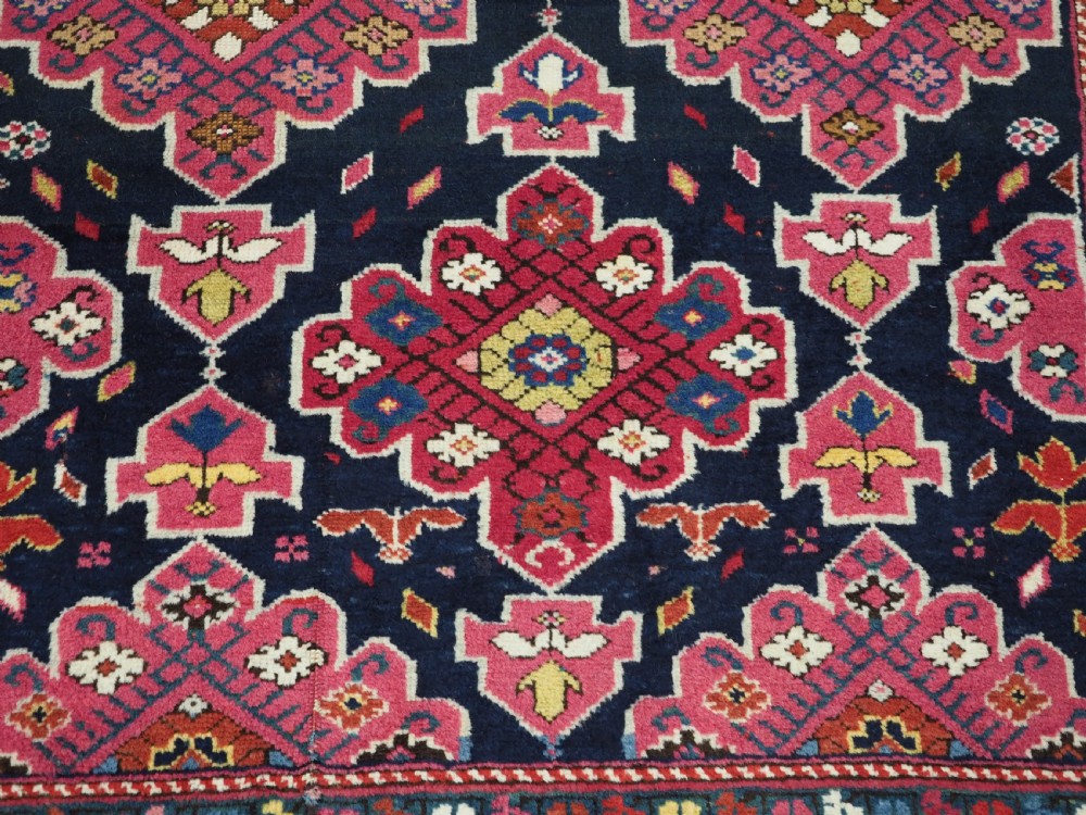 An antique long Caucasian runner rug featuring repeating pink and yellow geometric medallions on a dark navy field surrounded by a multi-band decorative border. View XXV